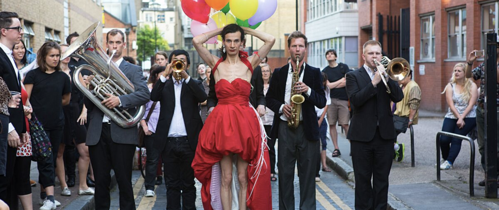 A person in a red dress with a parade behind them